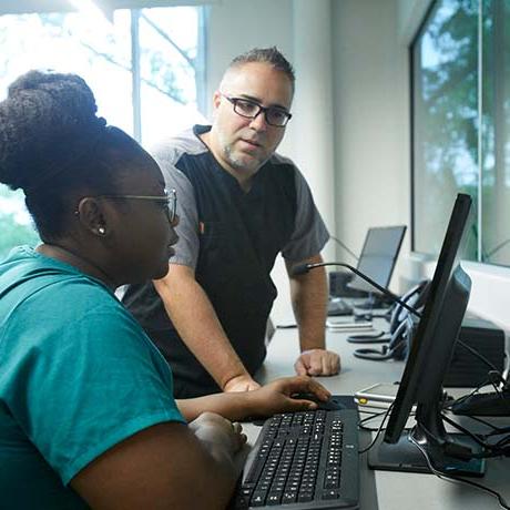 Two graduate nursing students work on a computer in the simulation lab